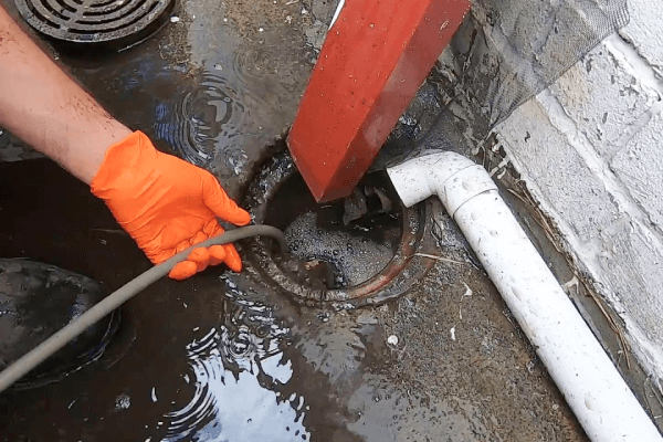 Plumber clearing blocked drain with hose to stop flooding, odours and hazards
